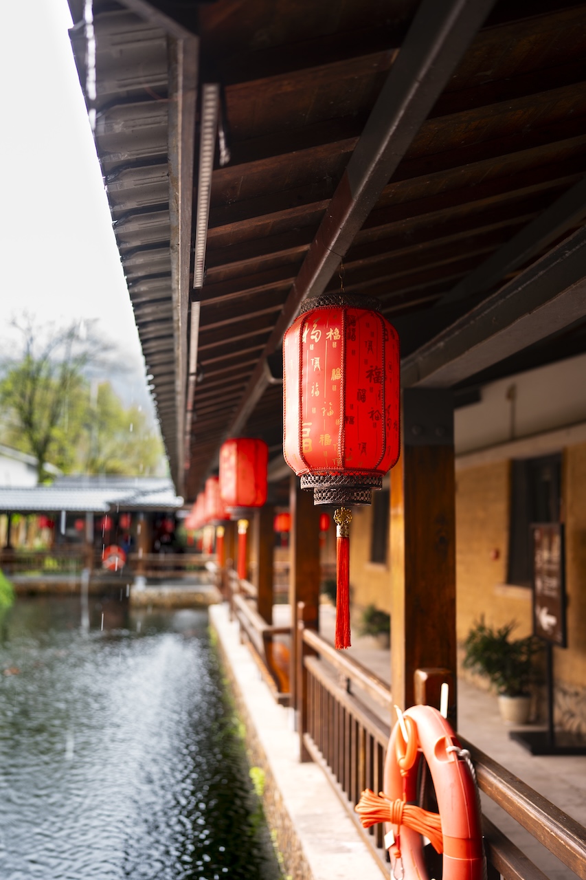 Red lanterns strung along a covered wooden walkway above the water.